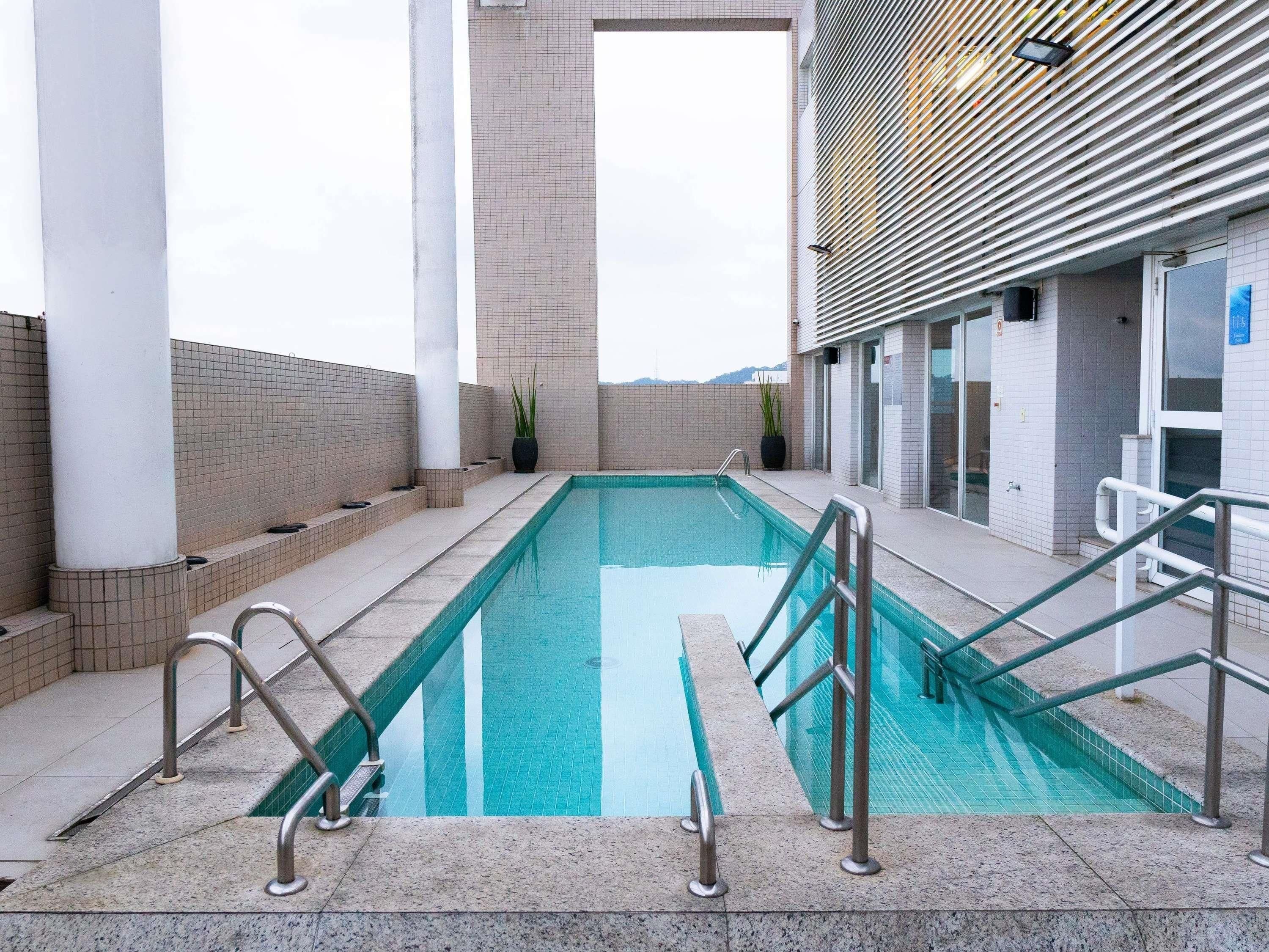 A swimming pool with a clear view of the sky, surrounded by a tiled deck and a building with a modern design.