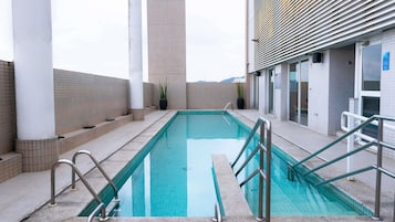 A swimming pool with a clear view of the sky, surrounded by a tiled deck and a building with a modern design.