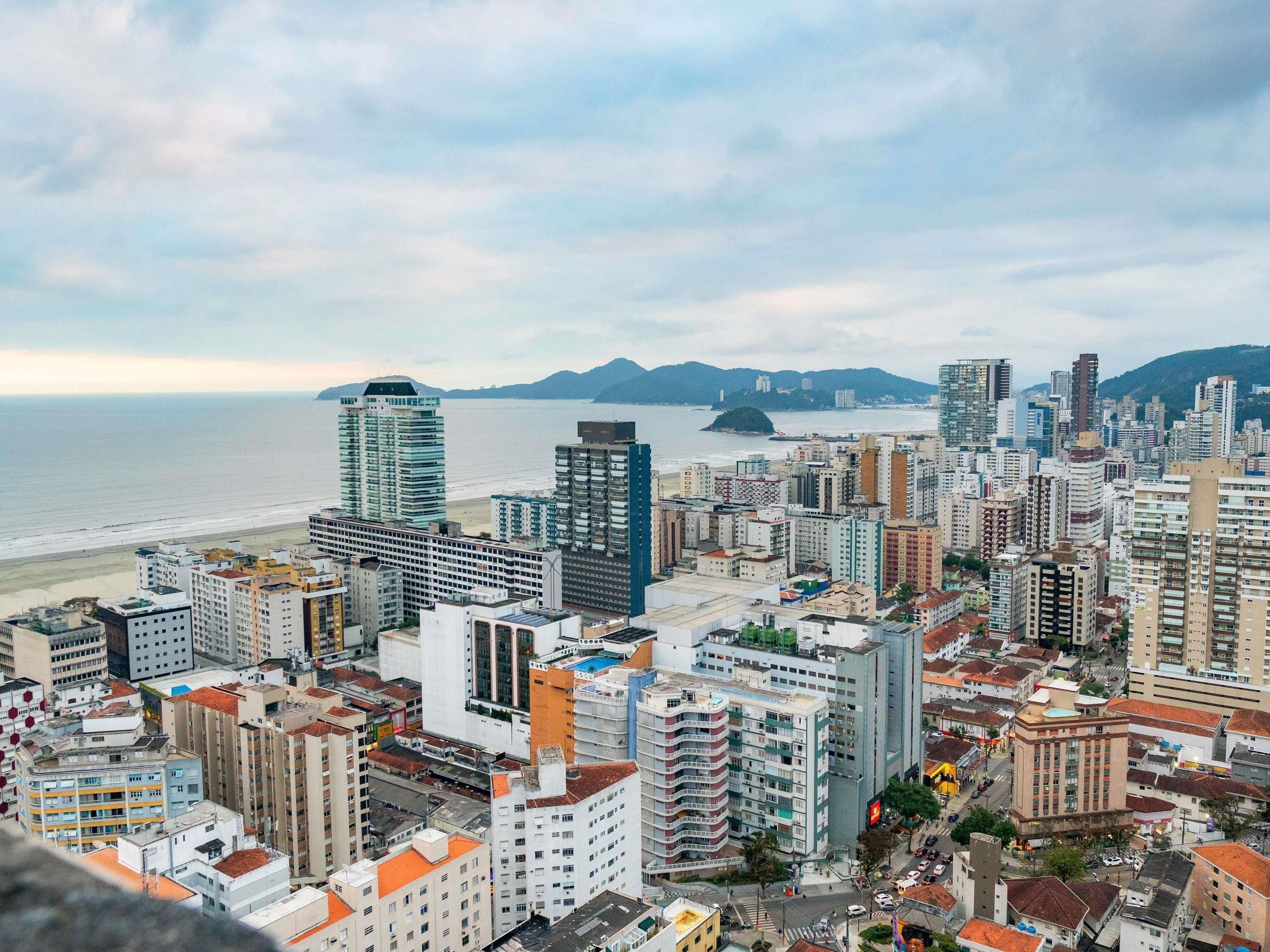 A cityscape with high-rise buildings, a beach, and mountains in the background.