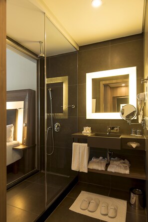 A modern bathroom with a glass-enclosed shower, a large mirror, and a vanity with towels and toiletries. - Novotel Santos Gonzaga (Santos)
