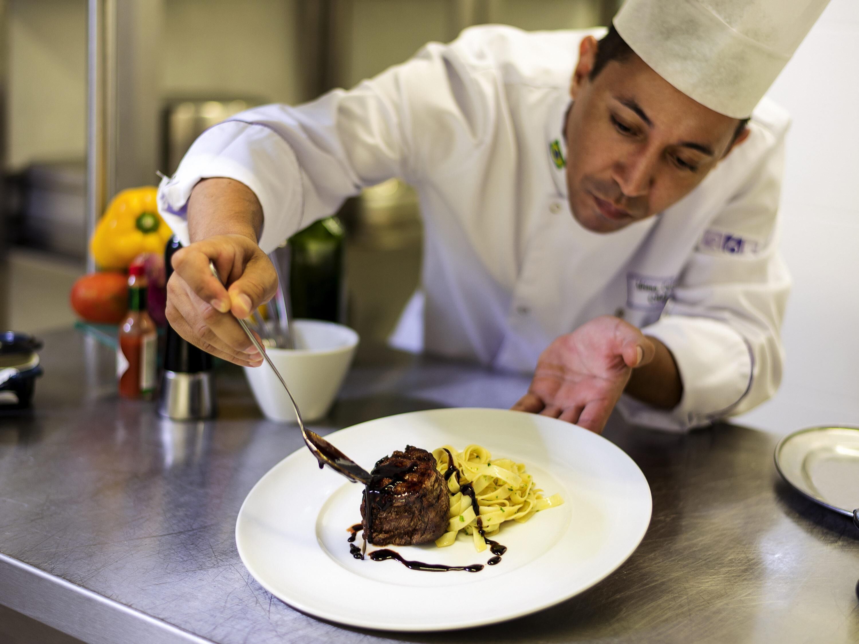 A chef preparing a dish on a stainless steel counter.