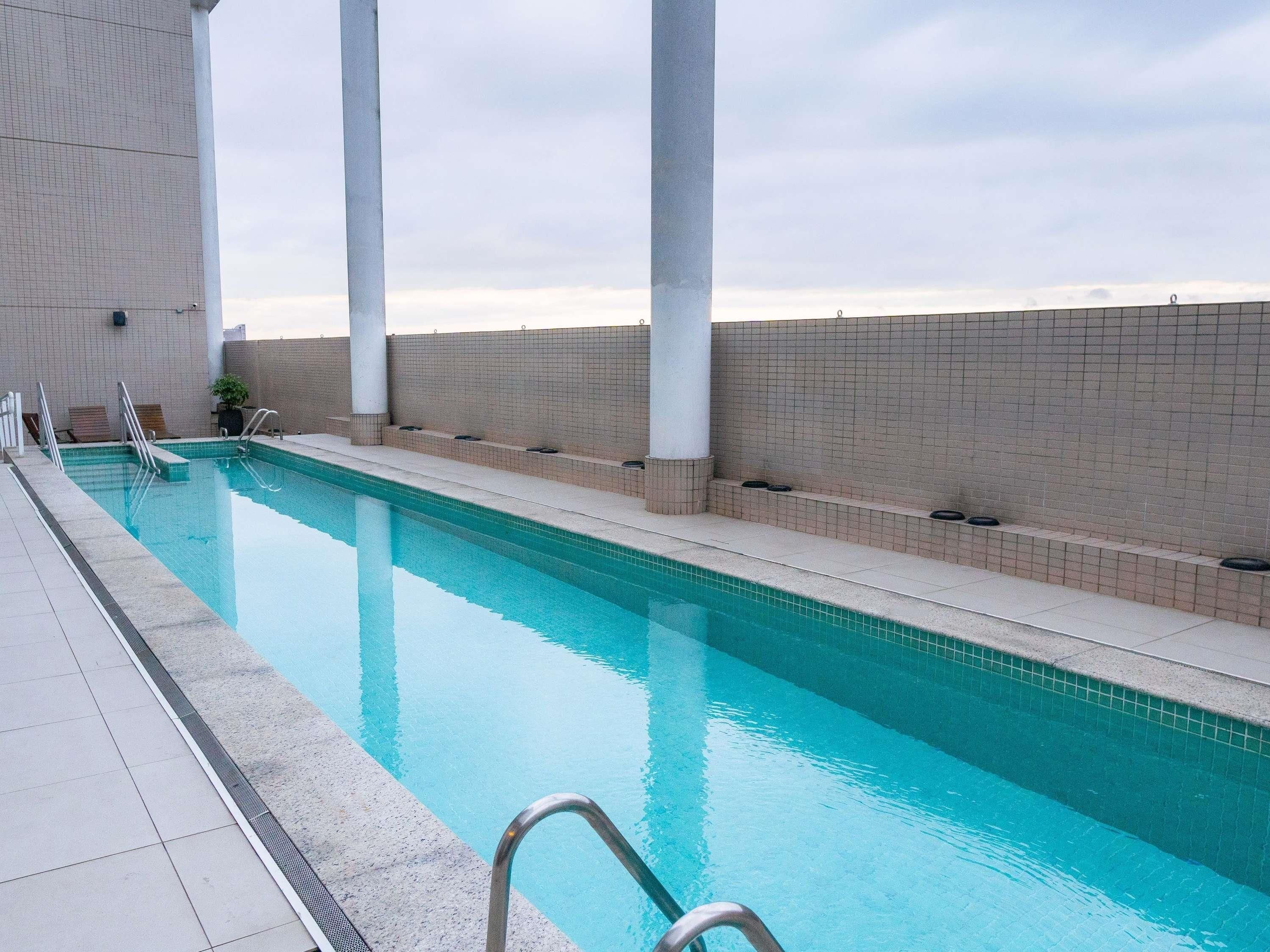 A swimming pool with a tiled edge, a metal handrail, and a tiled wall with a brick pattern.