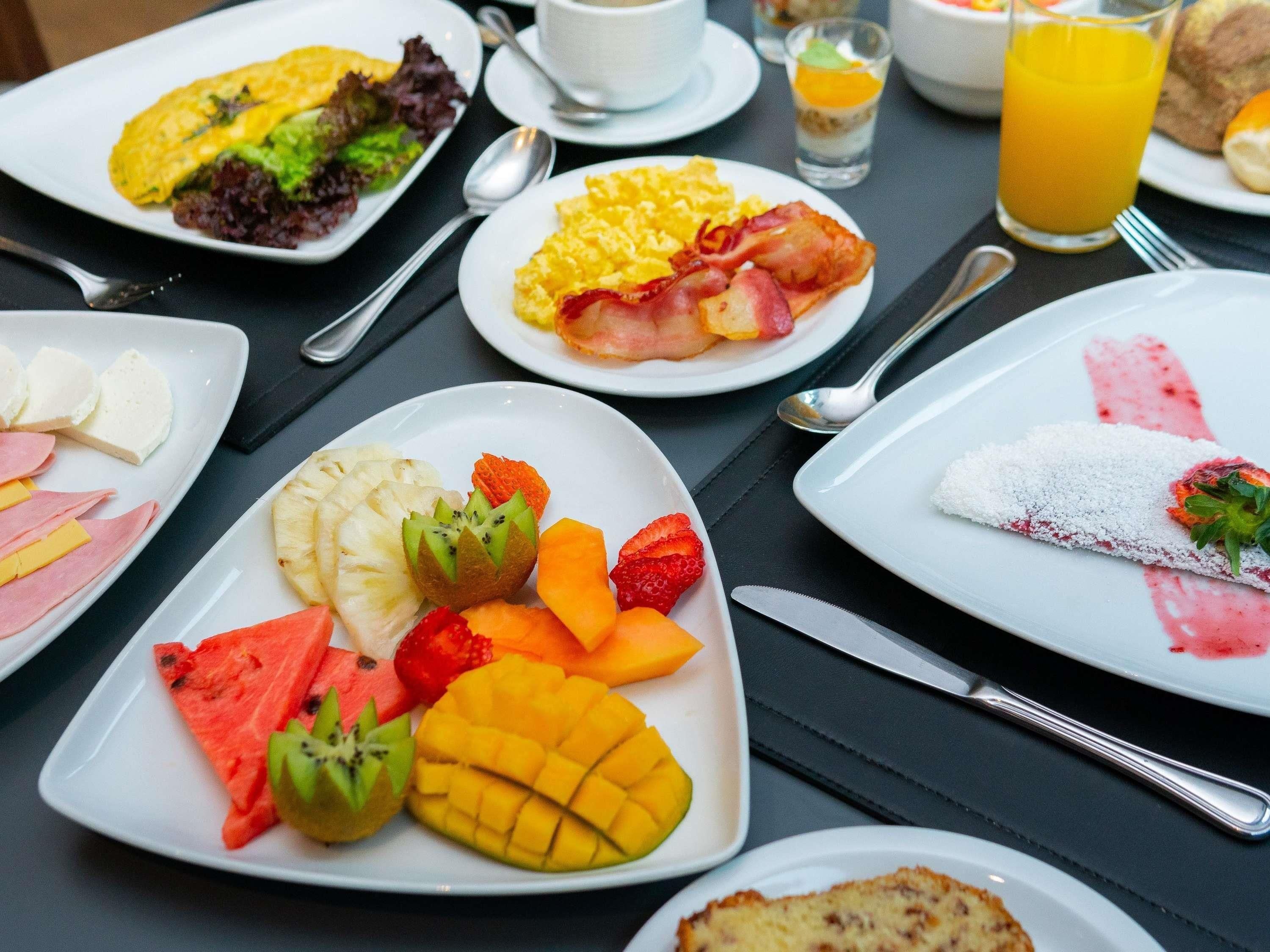 A breakfast buffet with various dishes including eggs, bacon, fruits, and pastries.