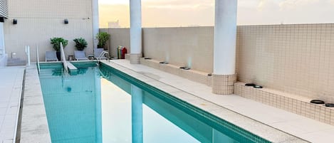 A swimming pool with a tiled edge, a white tiled wall, and a clear sky in the background.