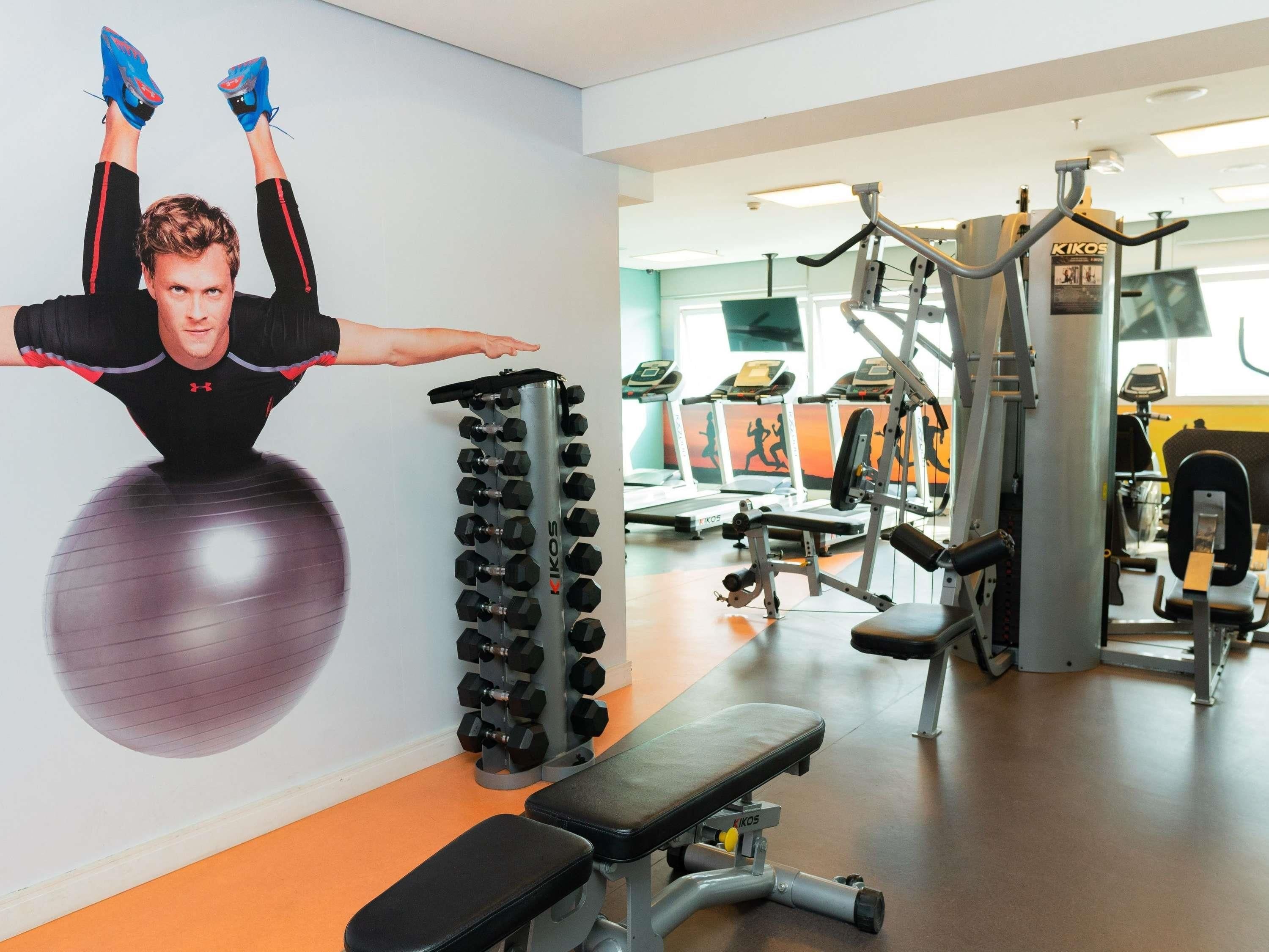 A gym with exercise equipment, a wall with a poster, and a bench.