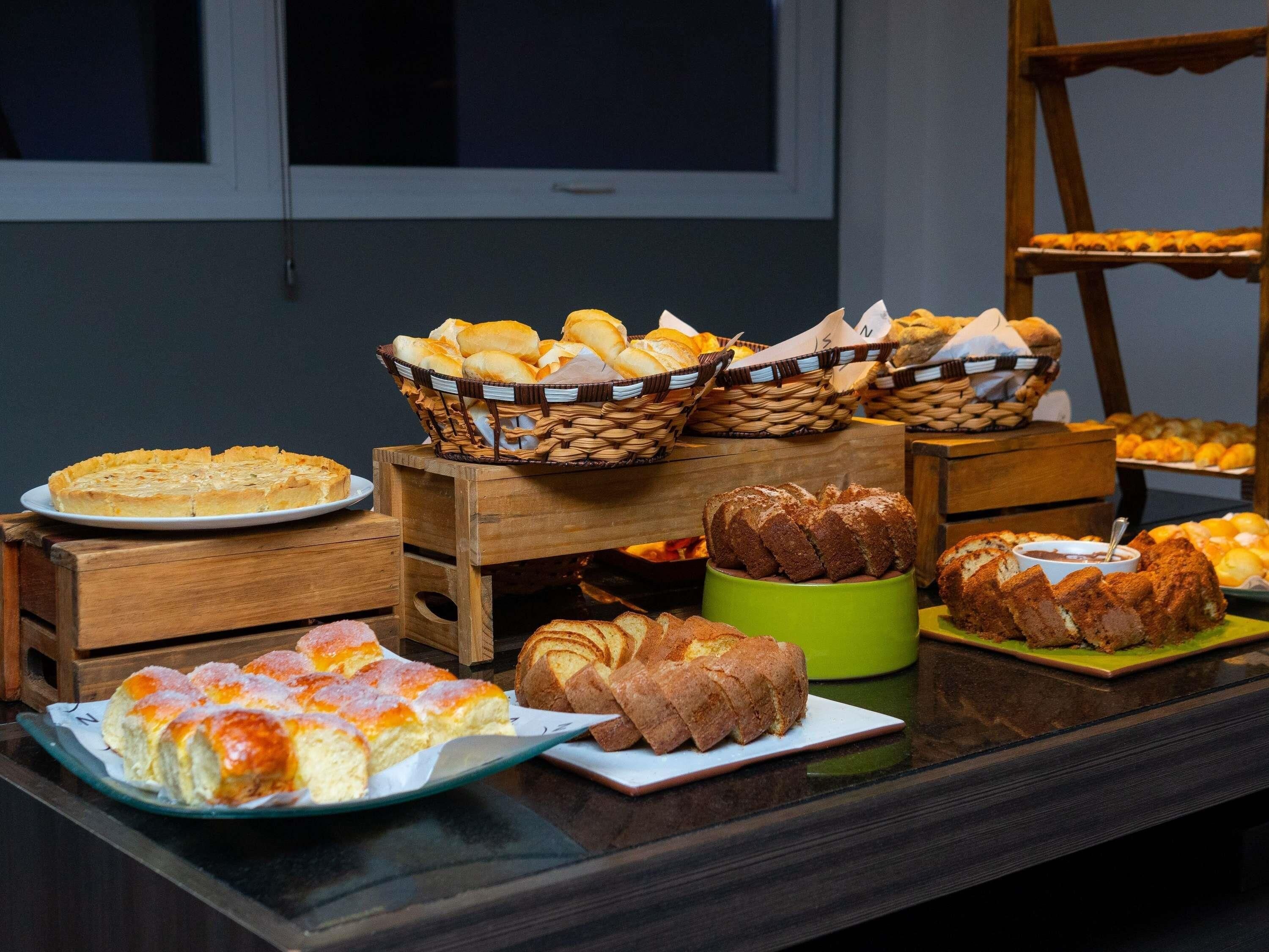 Una mesa de buffet con diversas opciones de panadería, incluyendo pan, pasteles y una tarta.