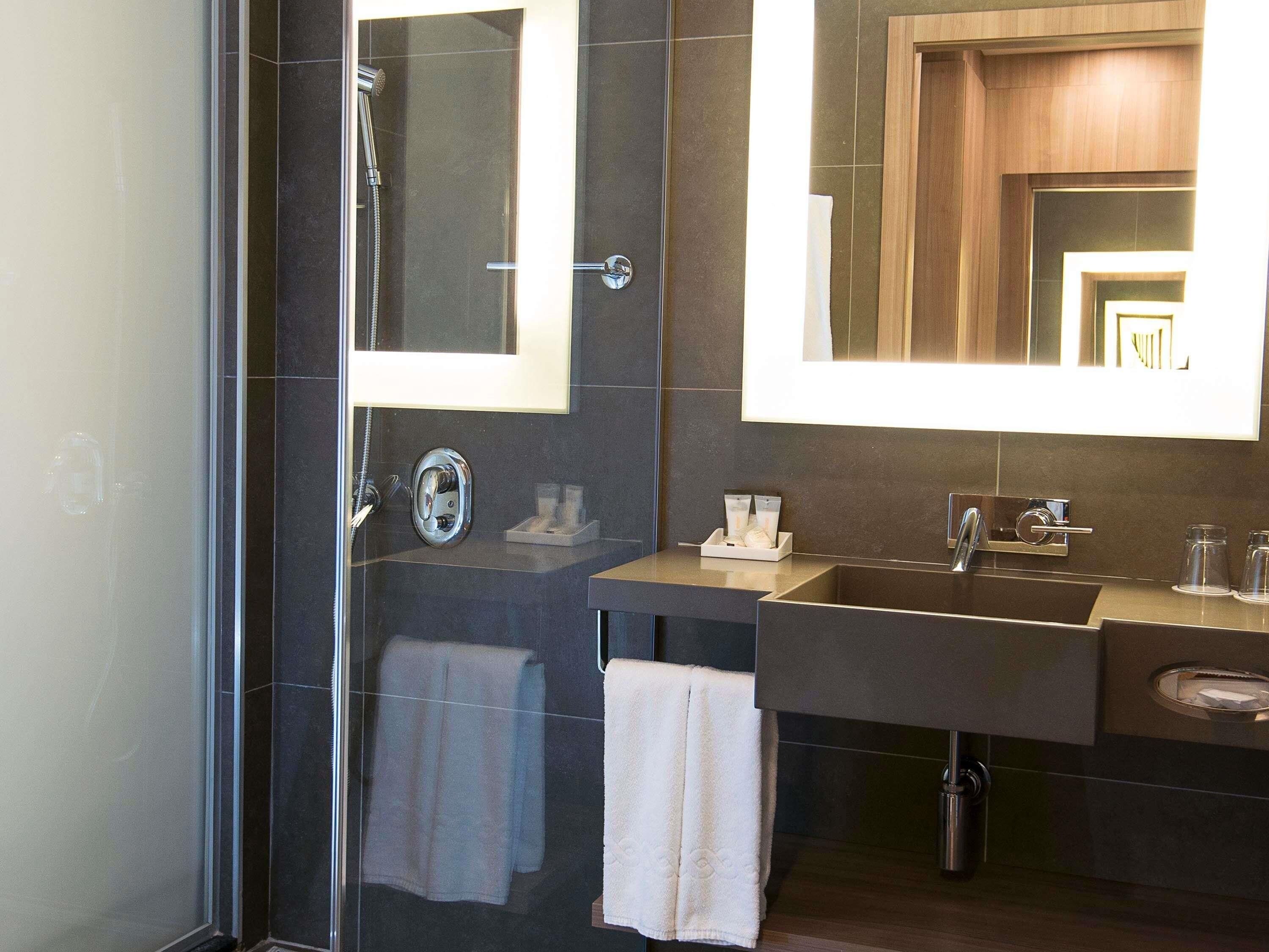 A modern bathroom with a glass-enclosed shower, a vanity with a sink, and a large mirror.