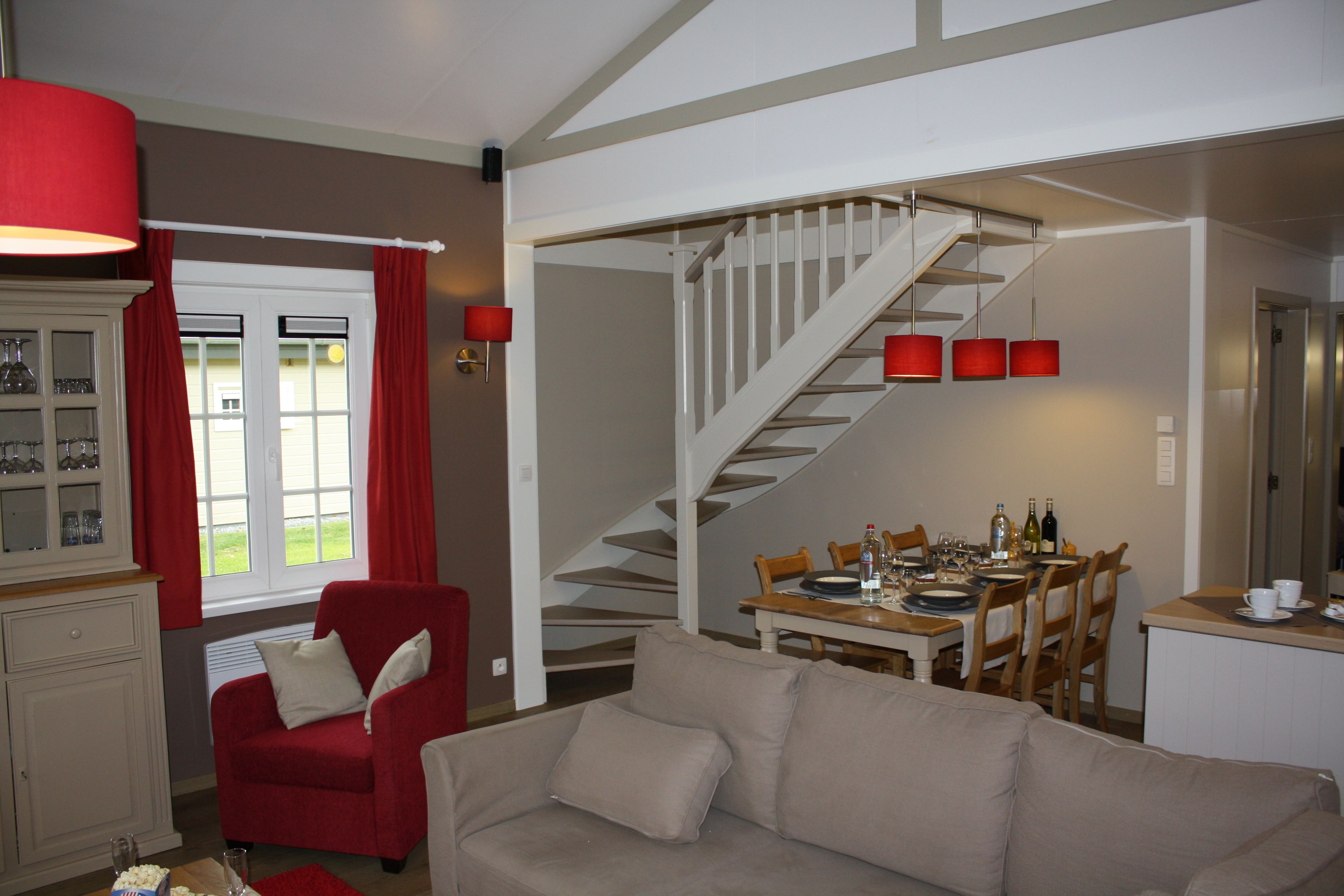 A living room with a red armchair, beige sofa, and a dining area with a staircase.