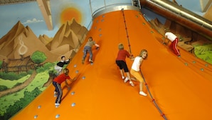 Kinder rutschen eine große Indoor-Rutsche, im Hintergrund eine Wandmalerei einer Landschaft.