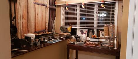 A kitchen with a wooden wall, a stove, a coffee maker, and a window with blinds.
