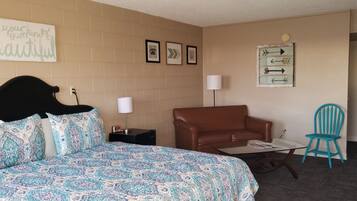 A bedroom with a bed, a brown sofa, a blue chair, a small table, and a wall with framed pictures and a sign.