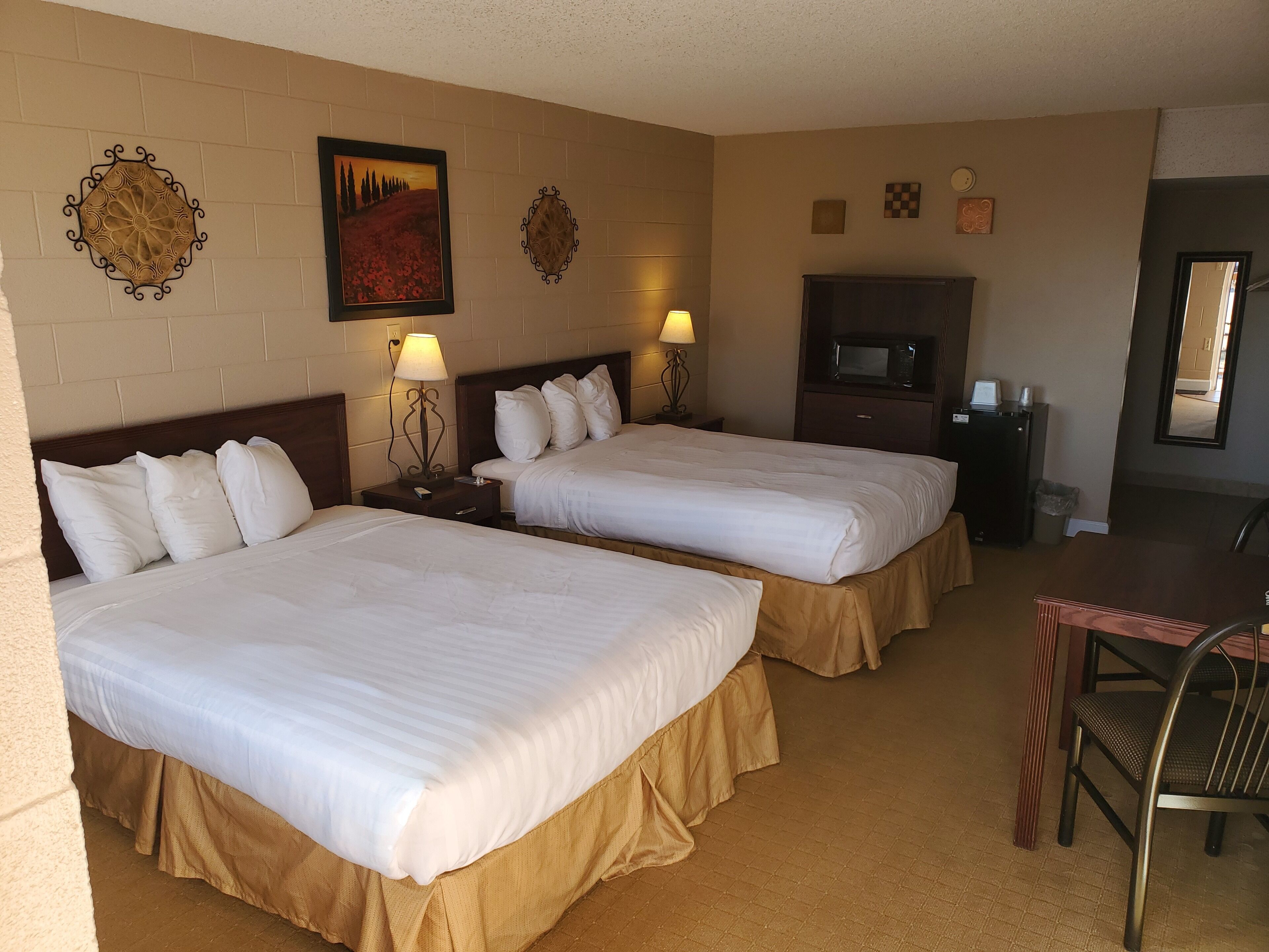 A hotel room with two beds, a desk, a chair, a TV, and decorative wall art.