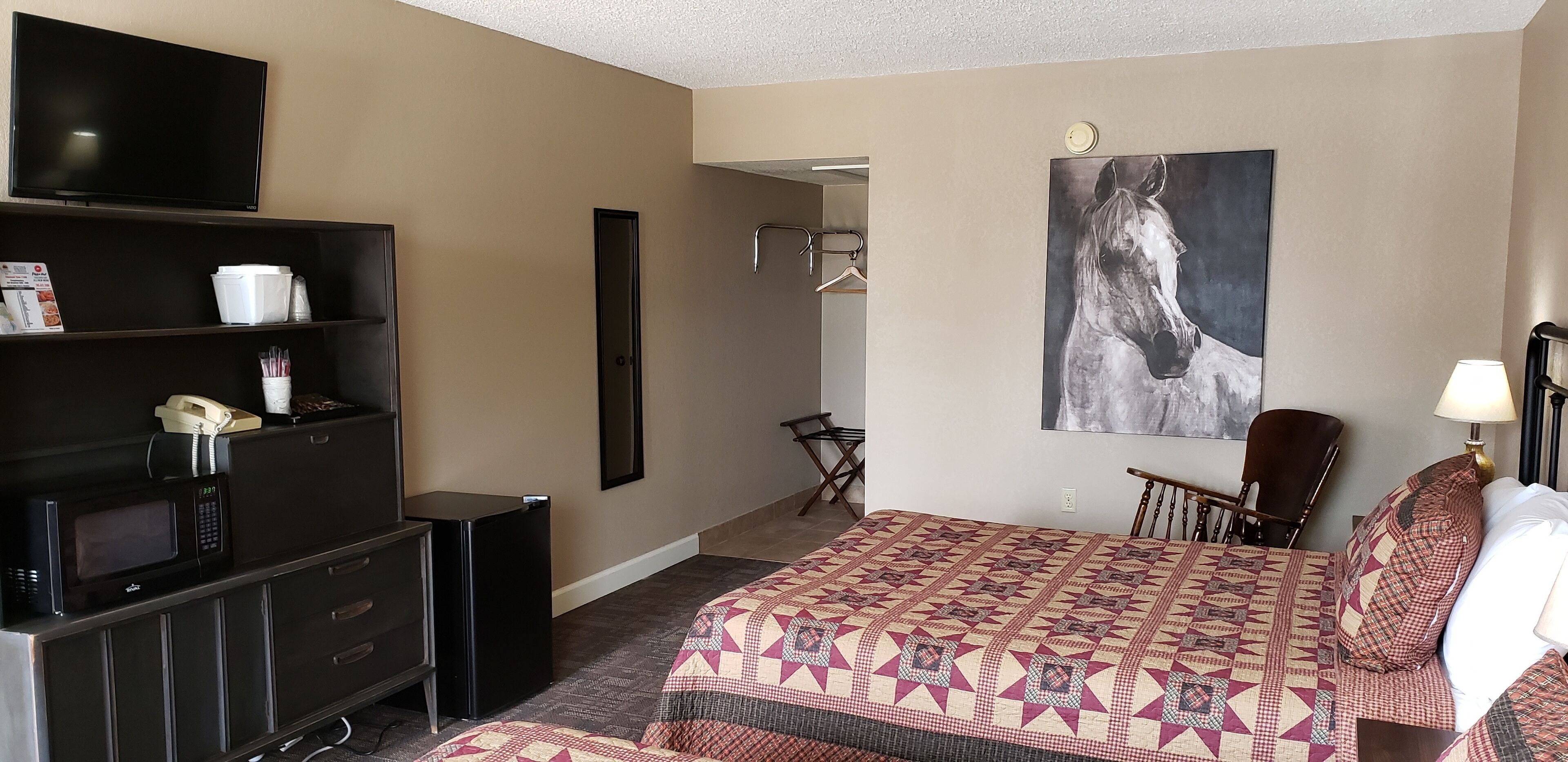 A hotel room with a bed, a TV, a microwave, a refrigerator, a chair, a desk, and a painting on the wall.