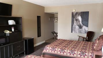 A hotel room with a bed, a TV, a microwave, a refrigerator, a chair, a desk, and a painting on the wall.