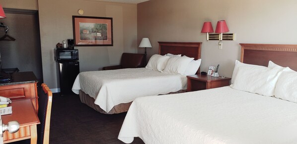 A hotel room with two beds, a desk, a chair, a TV, and a painting on the wall.