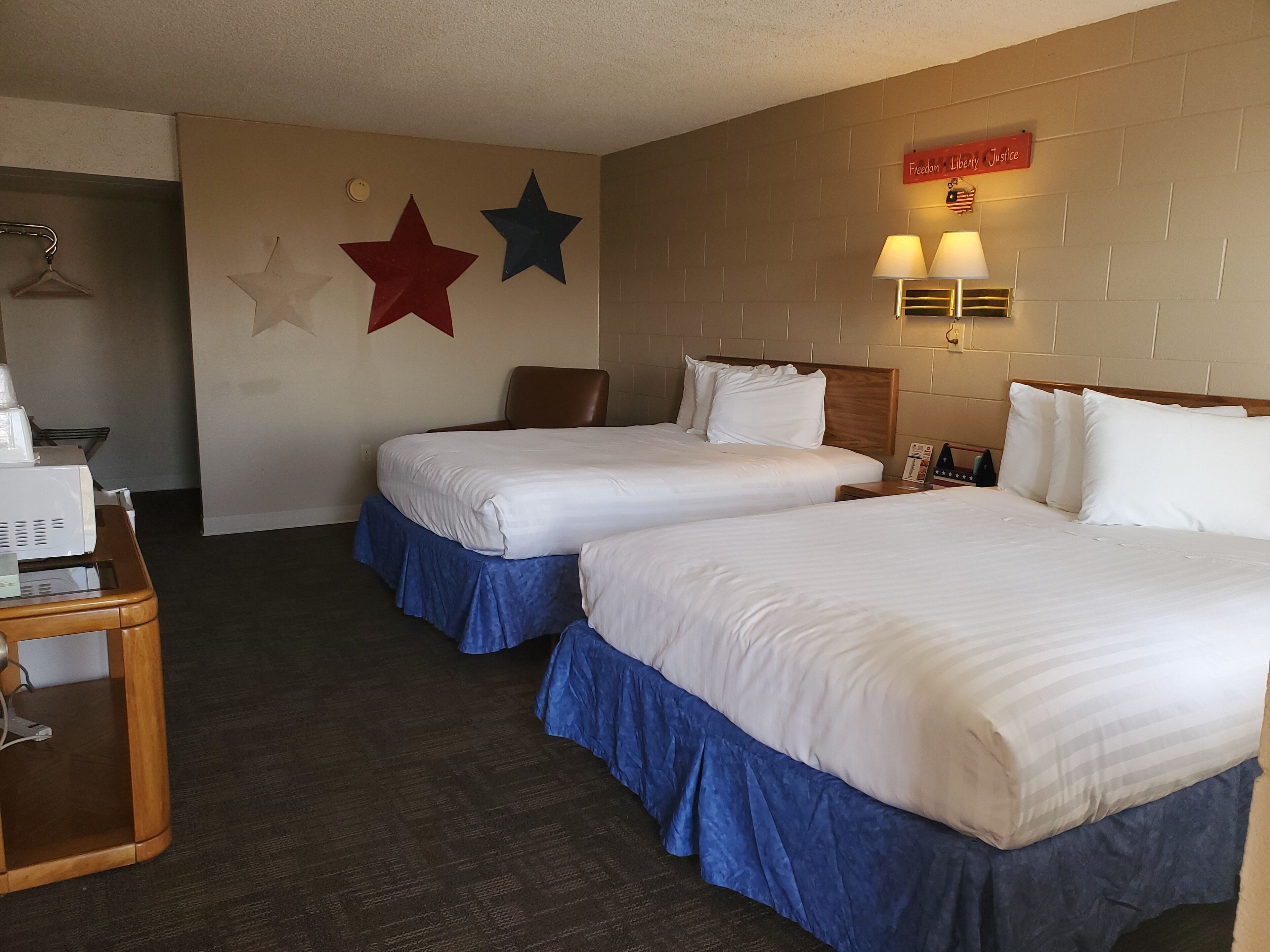 A hotel room with two beds, a desk with a microwave, and a wall with stars and a sign reading "Freedom Liberty Justice".