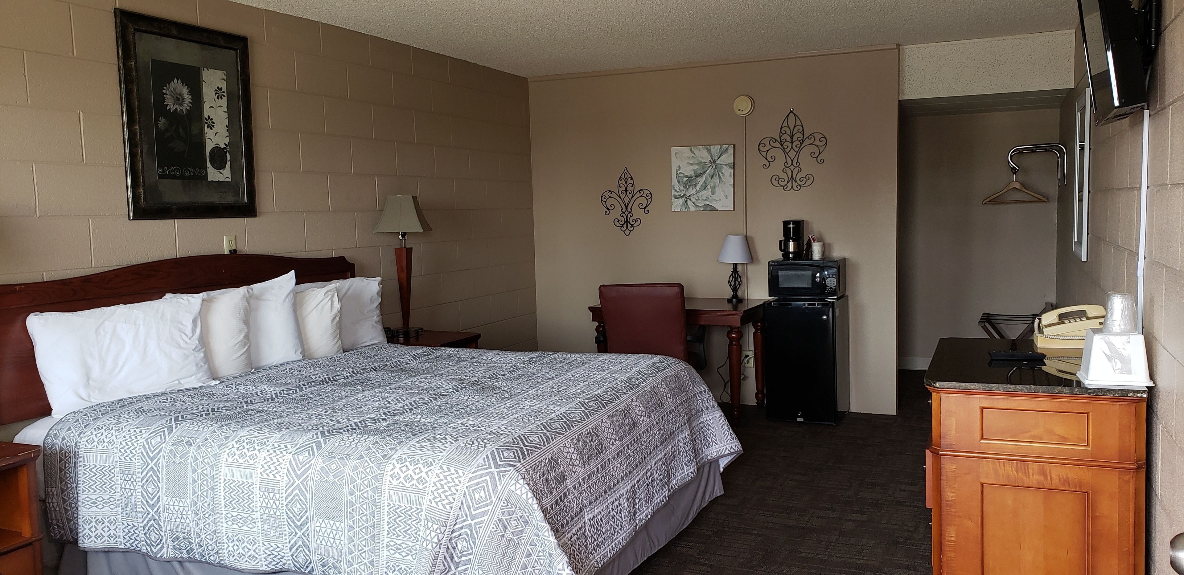 A hotel room with a bed, a desk, a chair, a microwave, a telephone, and a coat rack.
