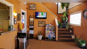 A hotel lobby with a television, framed artwork, a welcome sign, a staircase, and potted plants. - Kansas Country Inn (Oakley)