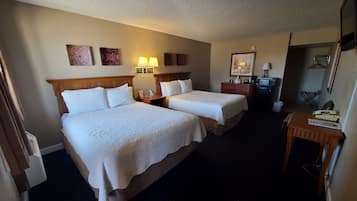 A hotel room with two beds, a desk, a chair, a lamp, and a small table.