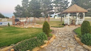 A gazebo, stone pathway, picnic tables, and a barbecue grill in a landscaped garden. - Kansas Country Inn (Oakley)
