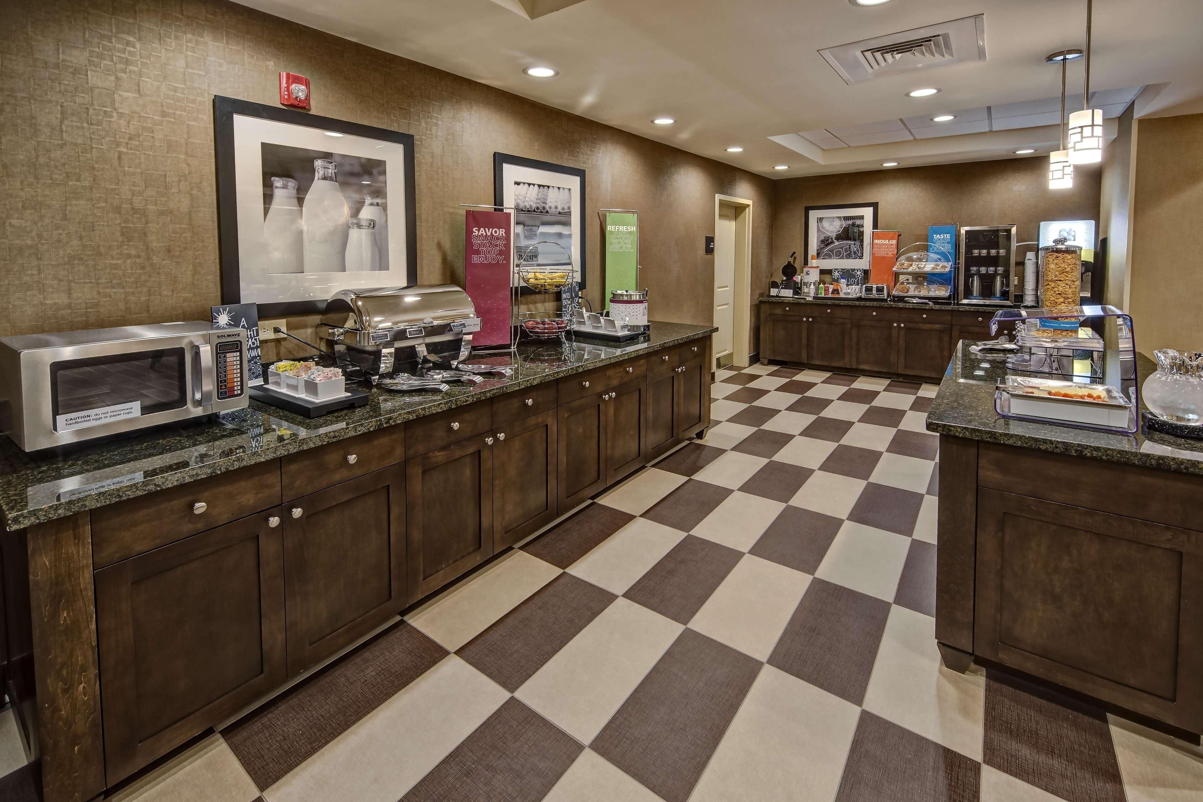 A hotel kitchen with a checkered floor, a microwave, a coffee machine, and various food dispensers.
