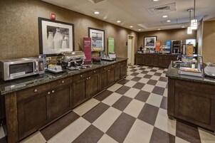 A hotel kitchen with a checkered floor, a microwave, a coffee machine, and various food dispensers.
