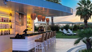 A bar area with a counter, bar stools, and a variety of bottles. There are lounge chairs and a palm tree in the background. - Radisson Blu Hotel Istanbul Ottomare (Istanbul)