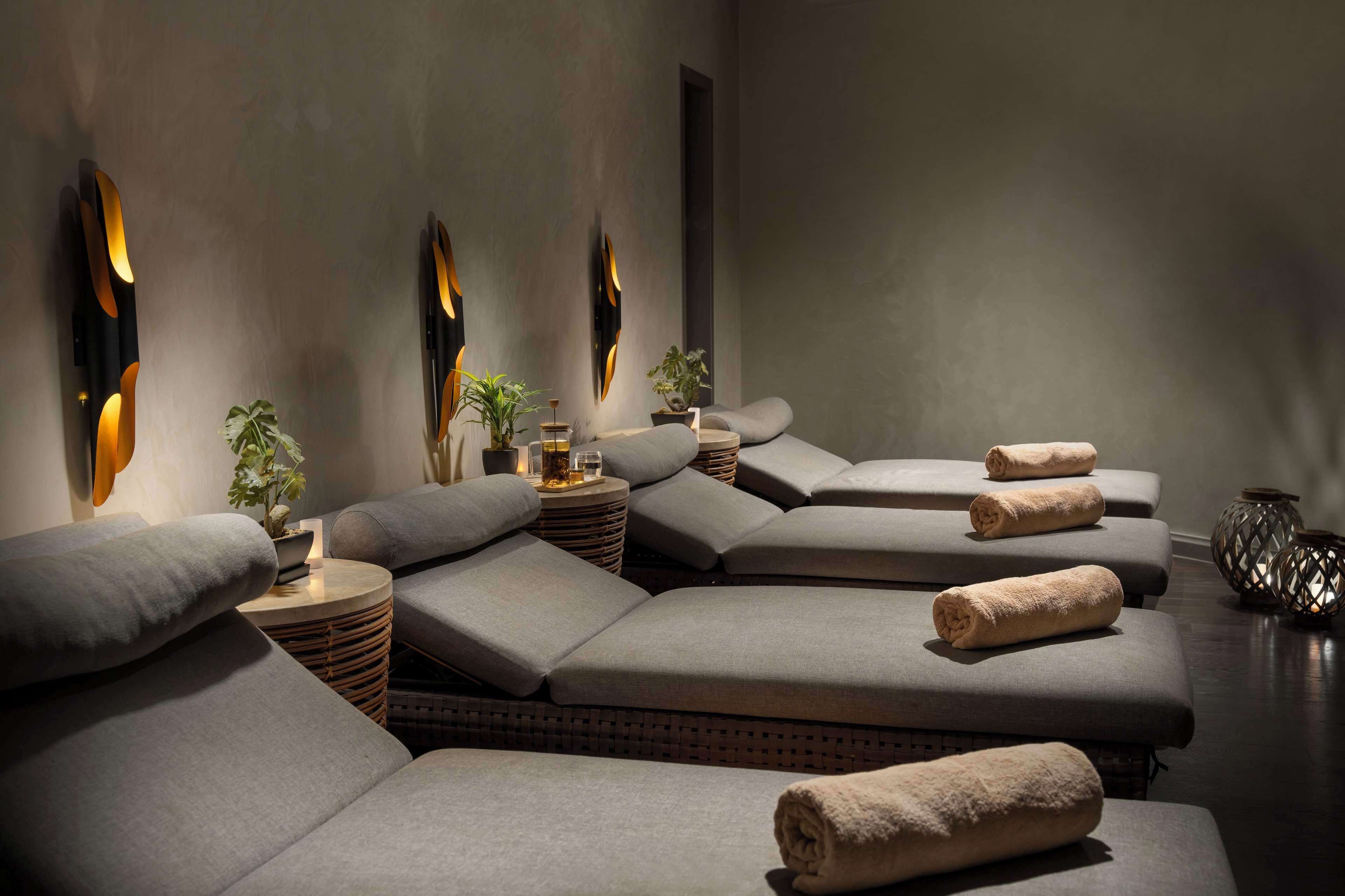 A modern spa room with multiple massage tables, ambient wall lighting, and small side tables with decorative items.