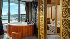Un baño moderno con una bañera grande, detalles de madera y vistas a un paisaje urbano a través de amplias ventanas.