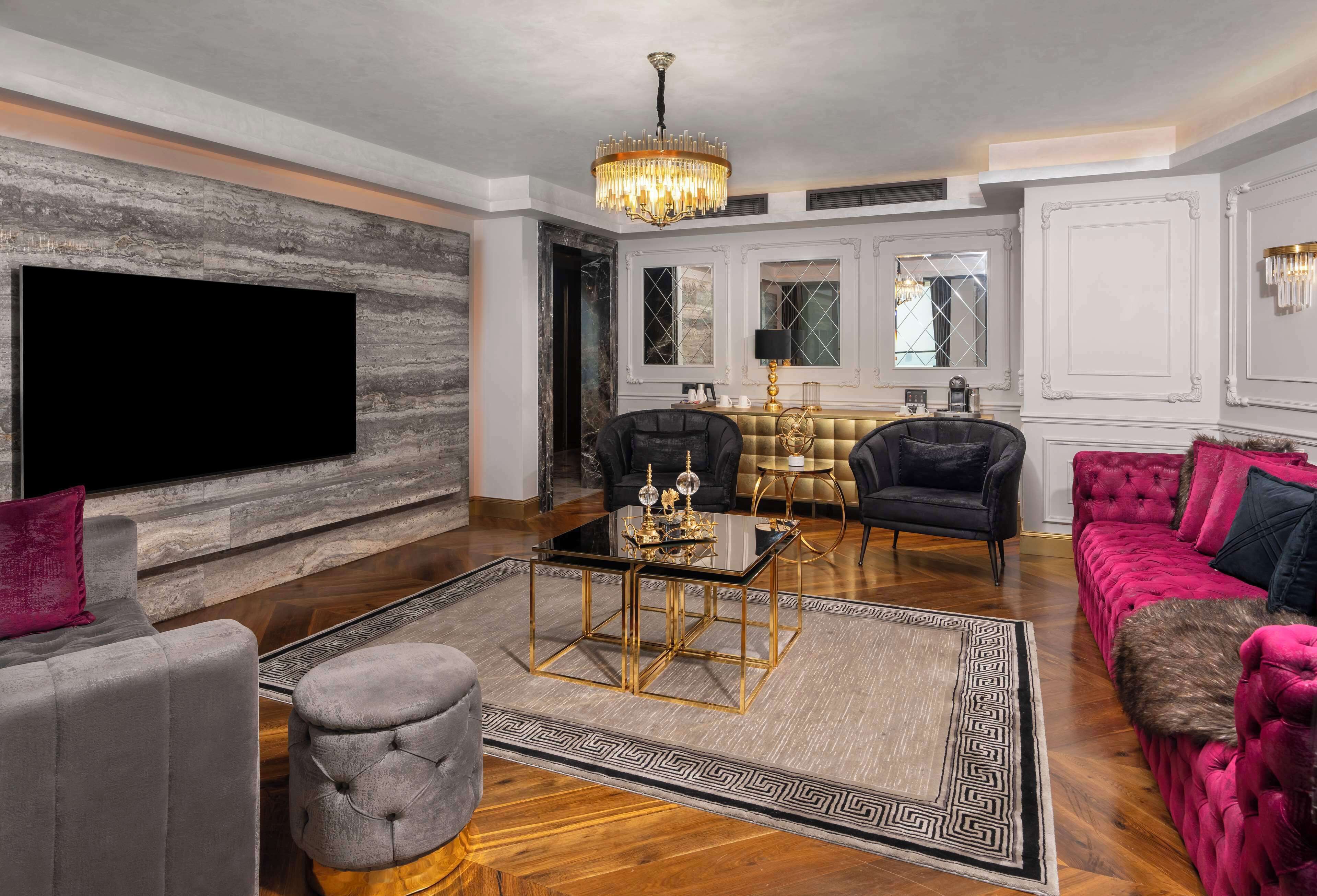 A spacious living room with a large flat-screen TV, a chandelier, and plush seating.