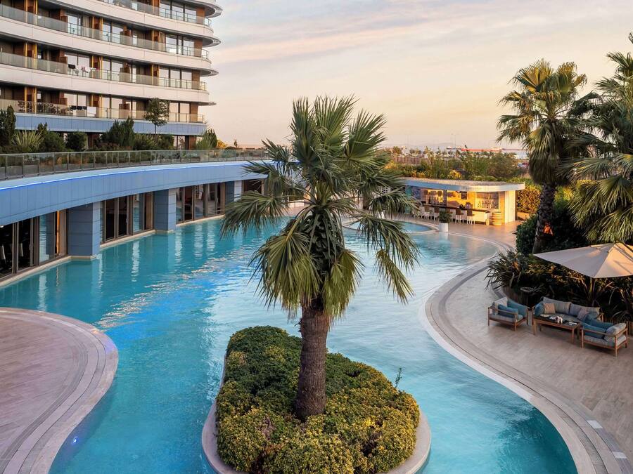 Un hôtel doté d’une grande piscine, de palmiers et d’un bâtiment moderne avec des balcons.