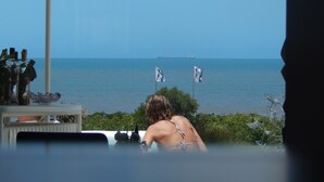 En person slapper af ved en pool med udsigt til havet og flag.