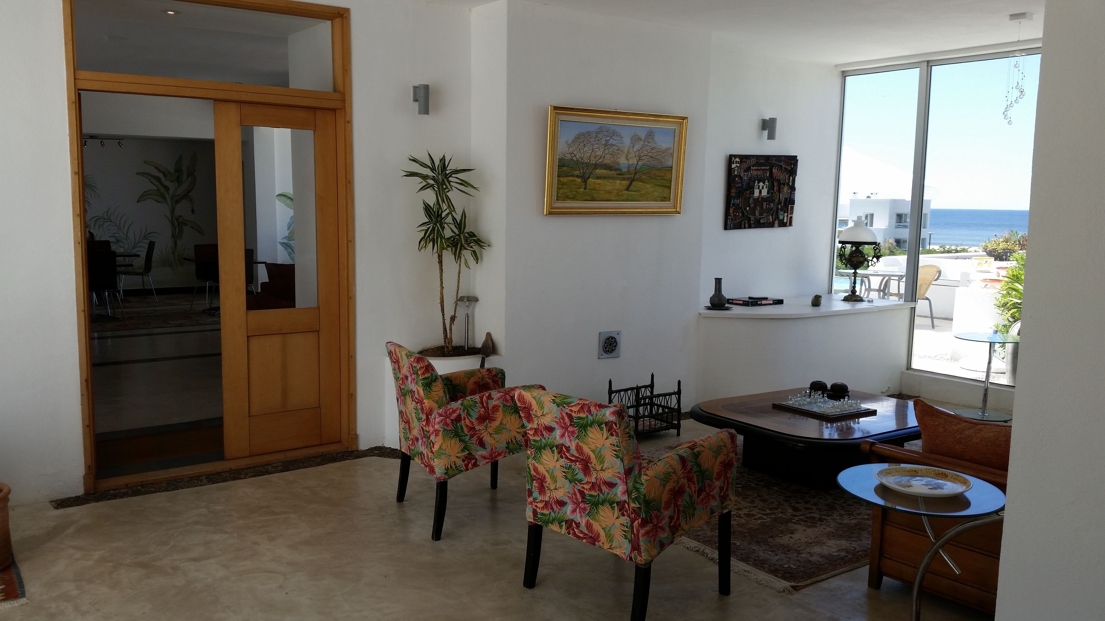 A dining area with a table and chairs, a potted plant, and a painting on the wall.