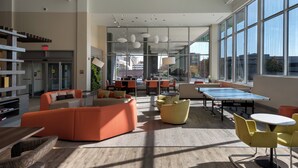 A modern hotel lobby with a ping pong table, orange and yellow seating, and large windows offering city views. - EVEN Hotel Omaha Downtown - Old Market by IHG (Omaha)