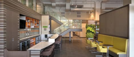 A modern bar area with a long counter, multiple stools, and a staircase leading to an upper level.