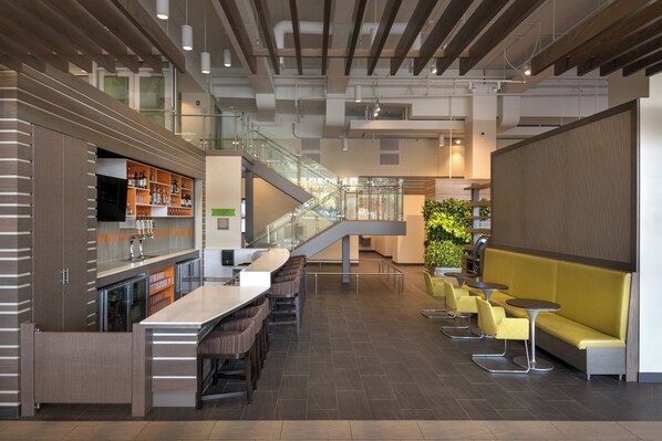 A modern bar area with a long counter, multiple stools, and a staircase leading to an upper level.