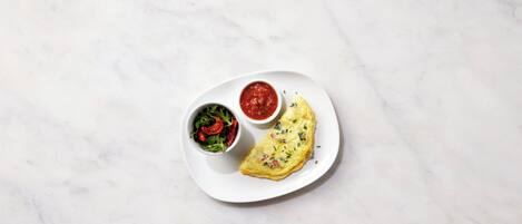 A white plate with an omelette, a bowl of salad, and a bowl of sauce on a marble surface.