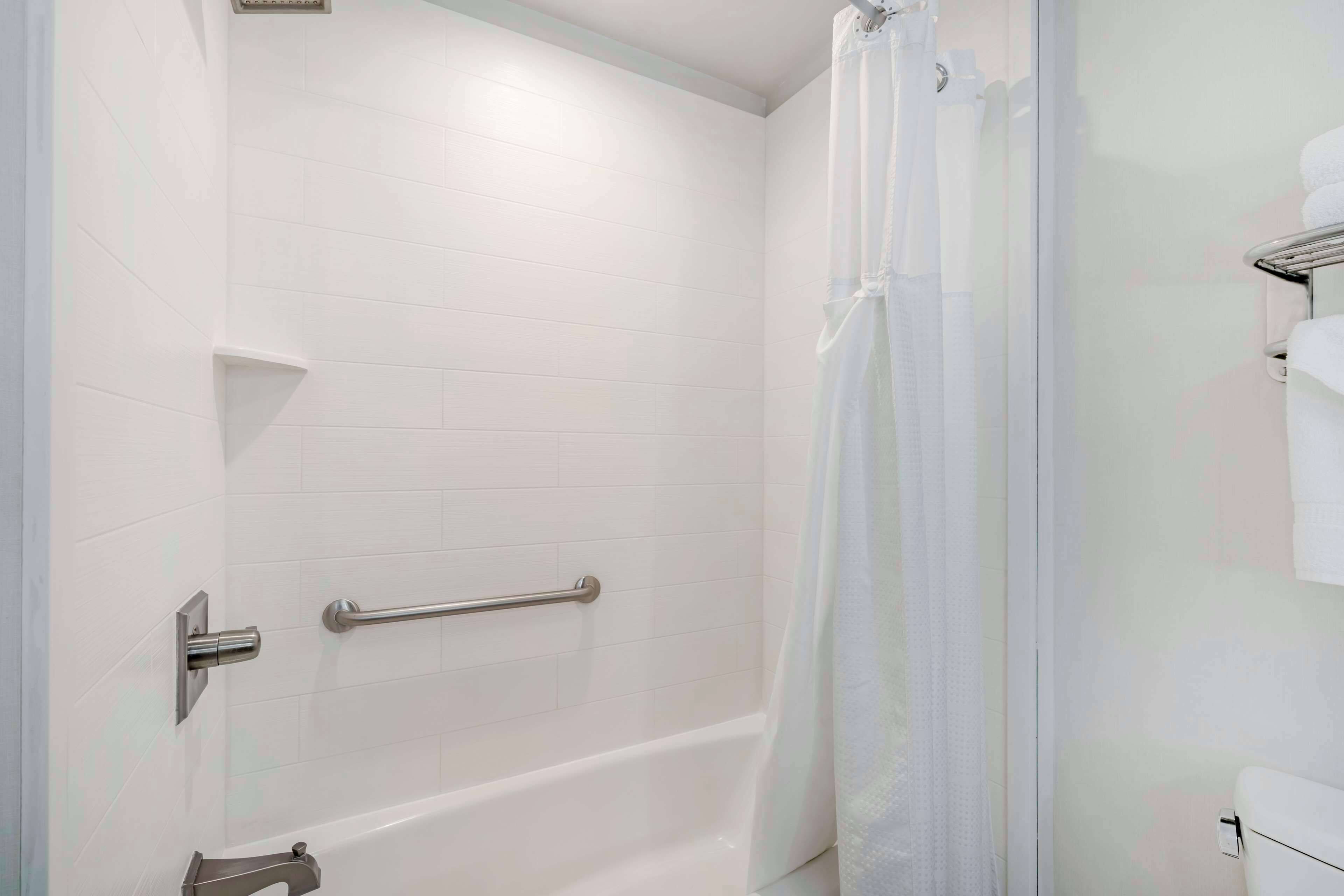A bathroom with white tiled walls, a white bathtub, a shower curtain, and a towel rack.