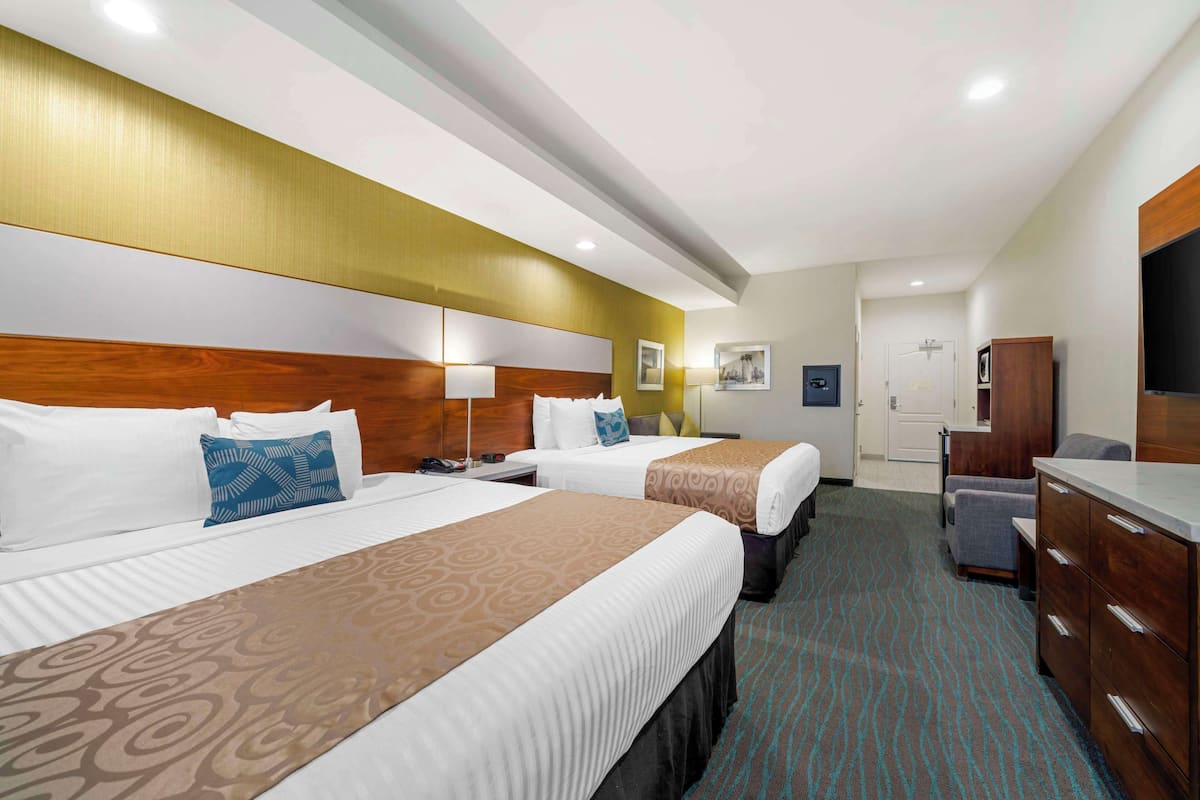 A hotel room with two beds, a wooden headboard, a flat-screen TV, a desk, and a wardrobe.