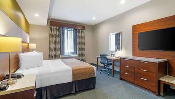 A hotel room with a bed, desk, chair, TV, and a large mirror.