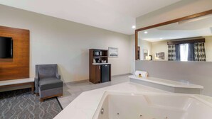 A modern bathroom with a large bathtub, a vanity with a mirror, and a seating area with a chair.
