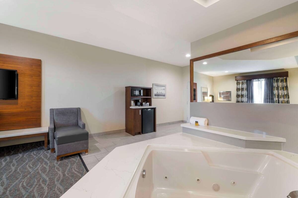 A modern bathroom with a large bathtub, a vanity with a mirror, and a seating area with a chair.