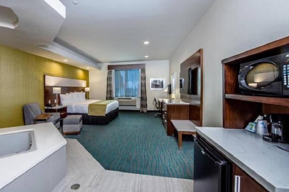 A hotel room with a large bed, a separate seating area, a desk, a bathroom with a bathtub, and a microwave.