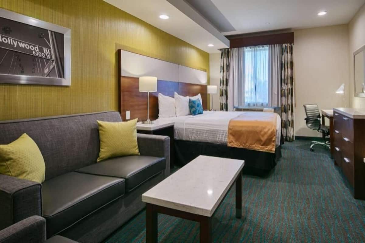 A hotel room with a bed, a sofa, a desk, a television, and a mirror.