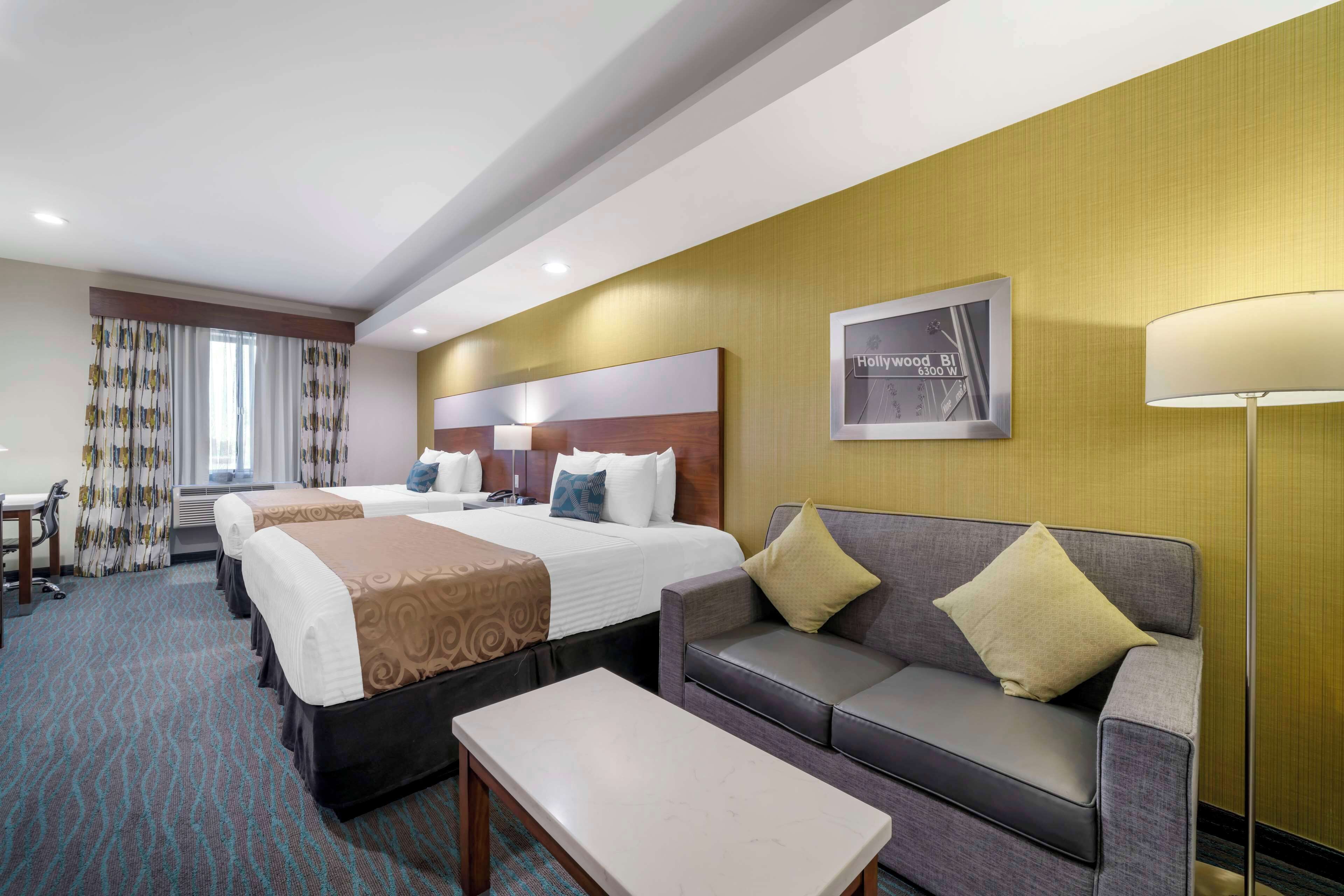 Hotellihuone, jossa on kaksi sänkyä, sohva, pöytä ja lamppu.