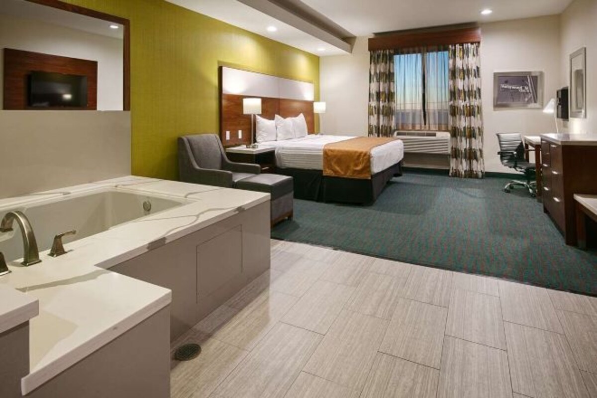 A hotel room with a large bathtub, a double bed, a desk, and a chair.