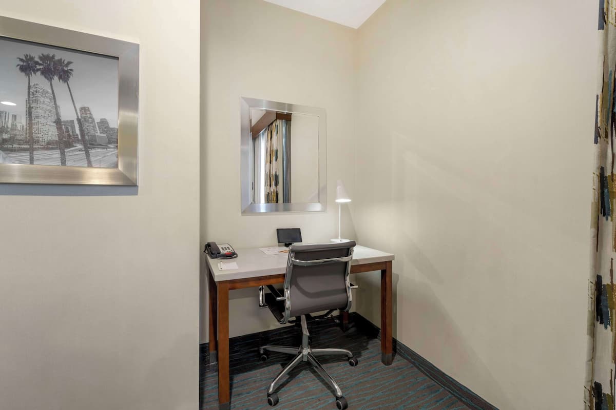 A hotel room with a desk, chair, and a mirror.