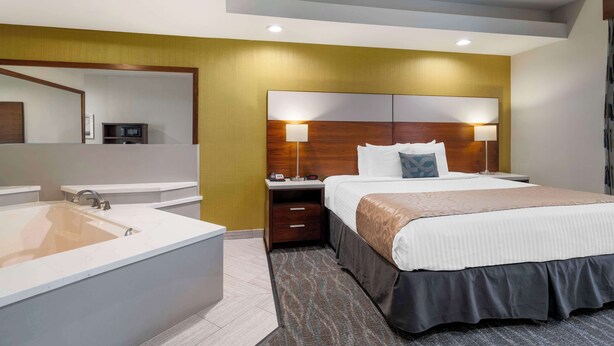 A modern hotel room with a large bed, a separate bathroom with a bathtub, a nightstand with a lamp, and a large mirror.