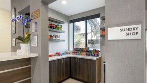 A reception area with a 'SUNDRY SHOP' sign, a reception desk, a potted plant, and shelves stocked with various products.