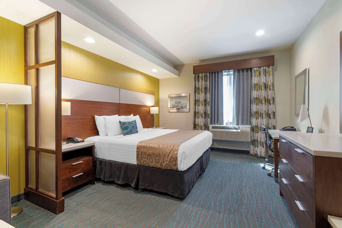 A hotel room with a large bed, a desk, a dresser, and a window with curtains.